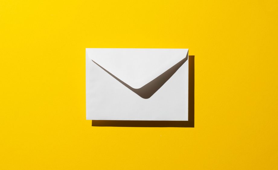 Envelope with harsh shadow over yellow background, top view